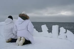 Two Inuit kneel on ice floe and look at the sky