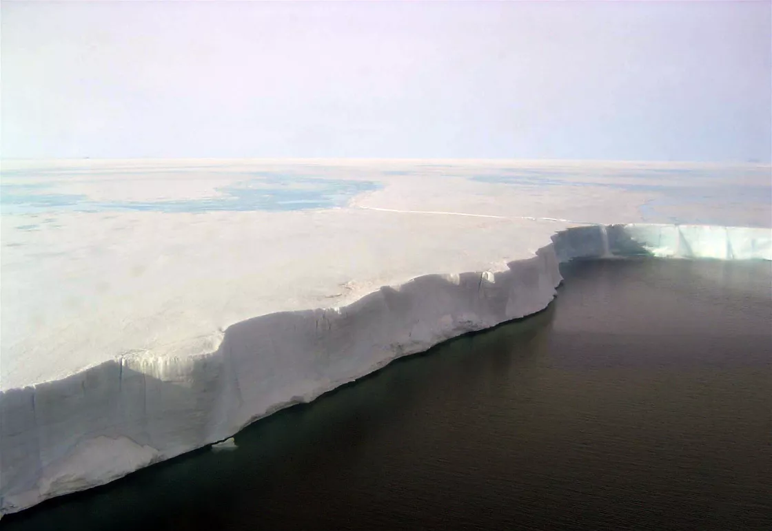 This in-flight photo shows the edge of the Larsen B Ice Shelf. The surface is melted, and ice flows off the edge like a waterfall. Photo Credit: Ted Scambos and Rob Bauer, NSIDC